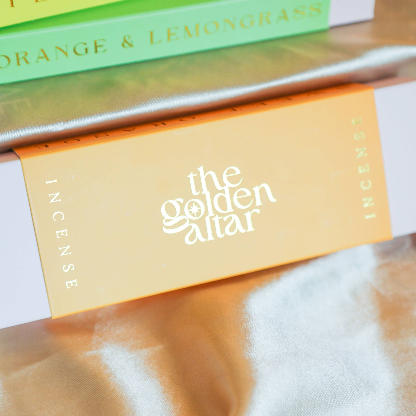 Eine orangefarbene Box von The Golden Altar mit 30 orangefarbenen Süße Orange Räucherstäbchen, die daneben liegen.