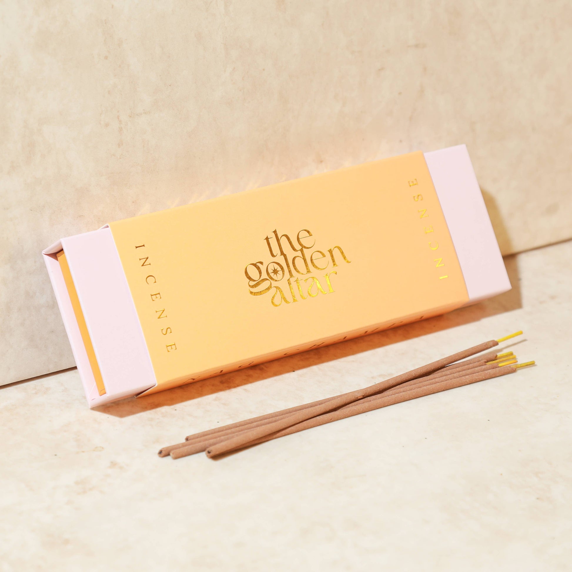 Eine pfirsichfarbene Box von The Golden Altar mit 30 Nag Champa Räucherstäbchen, die daneben liegen.