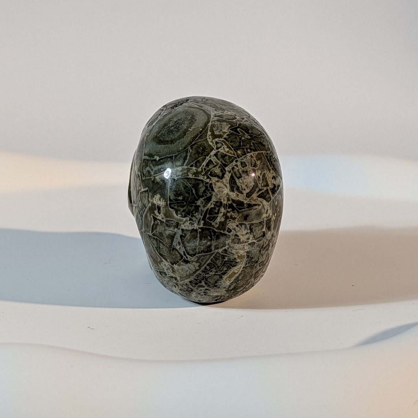 Gefährlich wirkender Kristallschädel Ilbertus aus tiefgrünem Serpentin 91g mit durchscheinenden, gelblichen Adern und harten Schatten