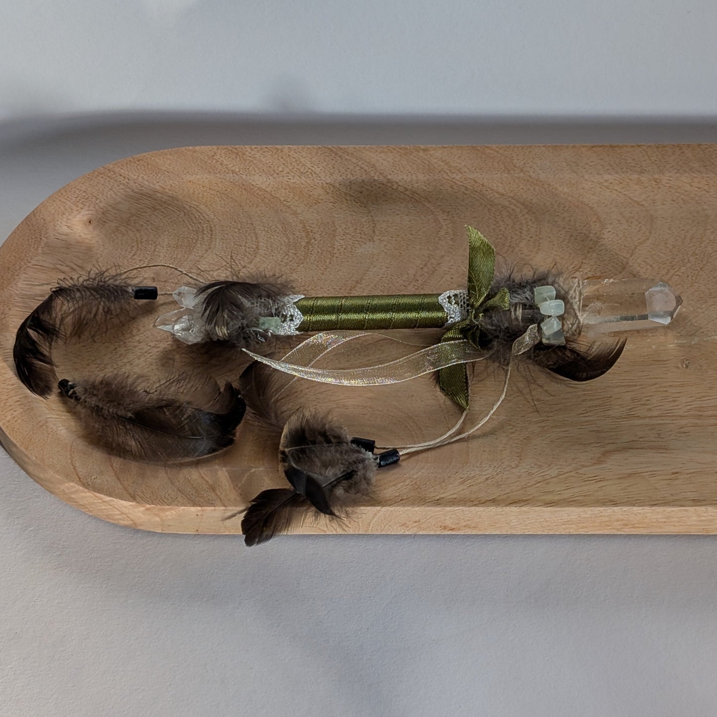 Handgefertigter Zauberstab mit einem goldgelben Citrin und schimmerndem Drusenquarz, verziert mit Federn und einem grünen Band, auf einer Holzplatte.