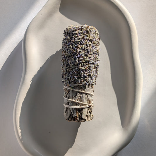 Handgemachtes Räucherbündel aus Weißem Salbei, umhüllt von Lavendelblüten, in einer weißen Keramikschale.