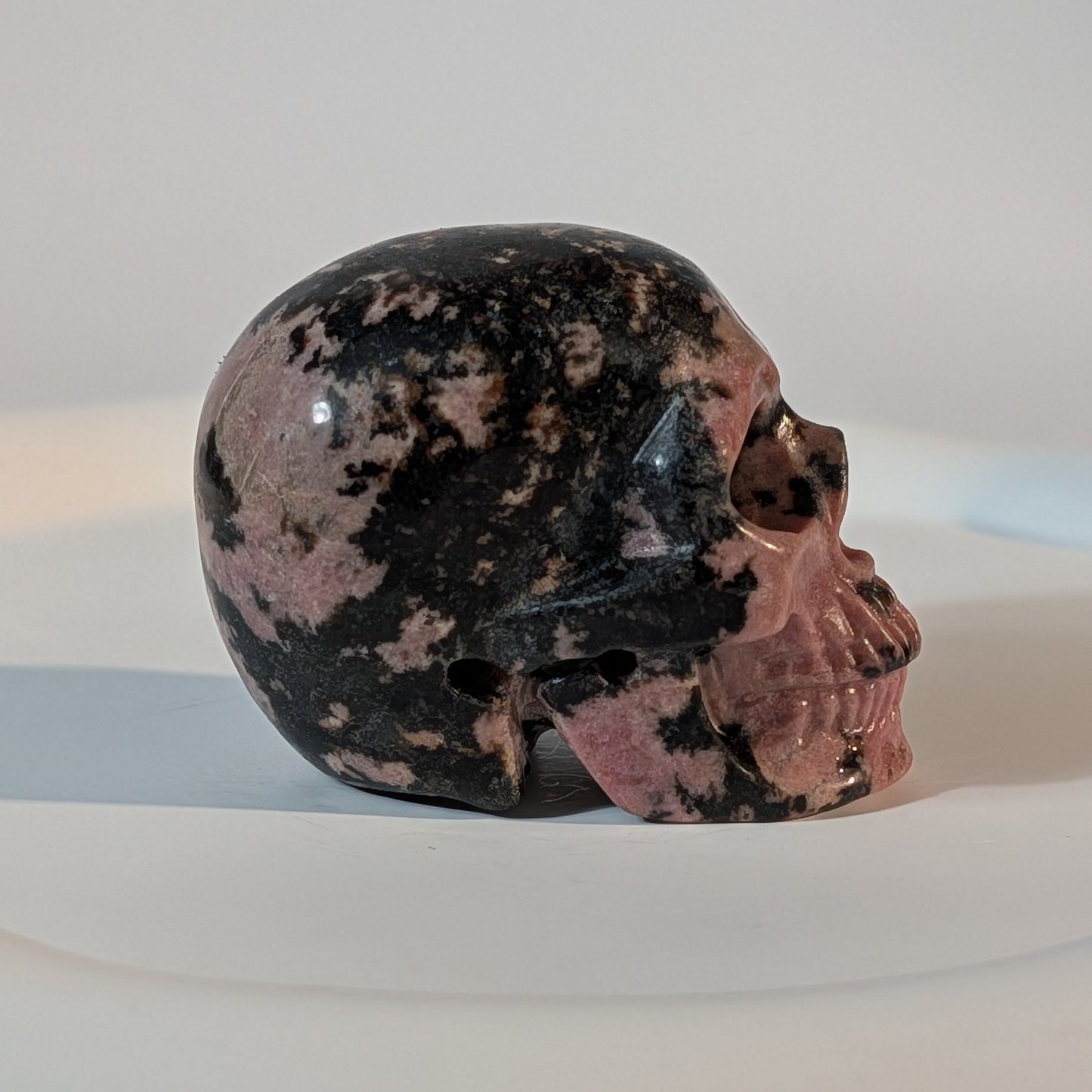 Handgeschnitzter Kristallschädel Sariel aus echtem Rhodonit, 114 Gramm schwer, mit markanter rosa-schwarzer Maserung für emotionale Heilung und Erdung.