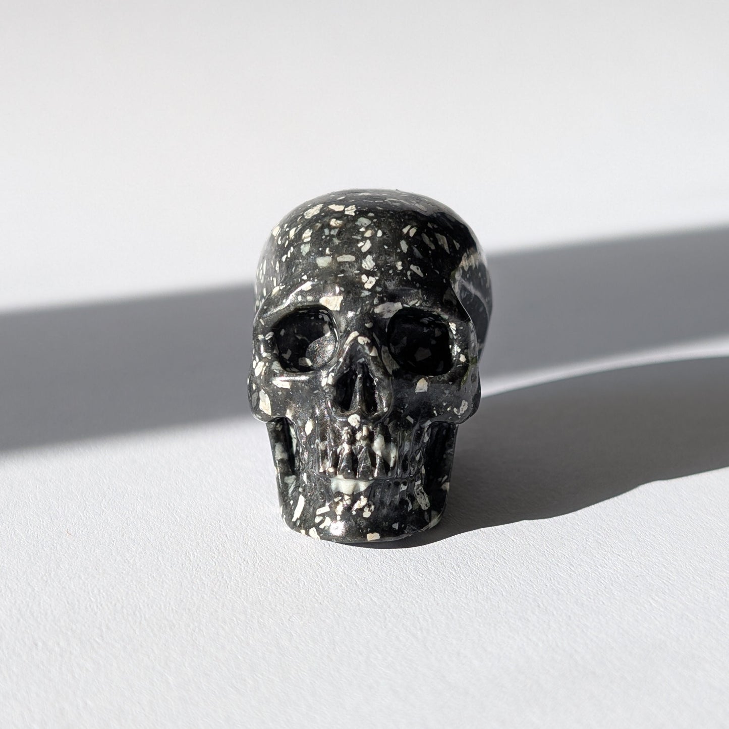 Kleiner Kristallschädel "Blyss" (87g) aus dunkelgrauem Gabbro (Mystic Merlinite) mit hellen Sprenkeln.