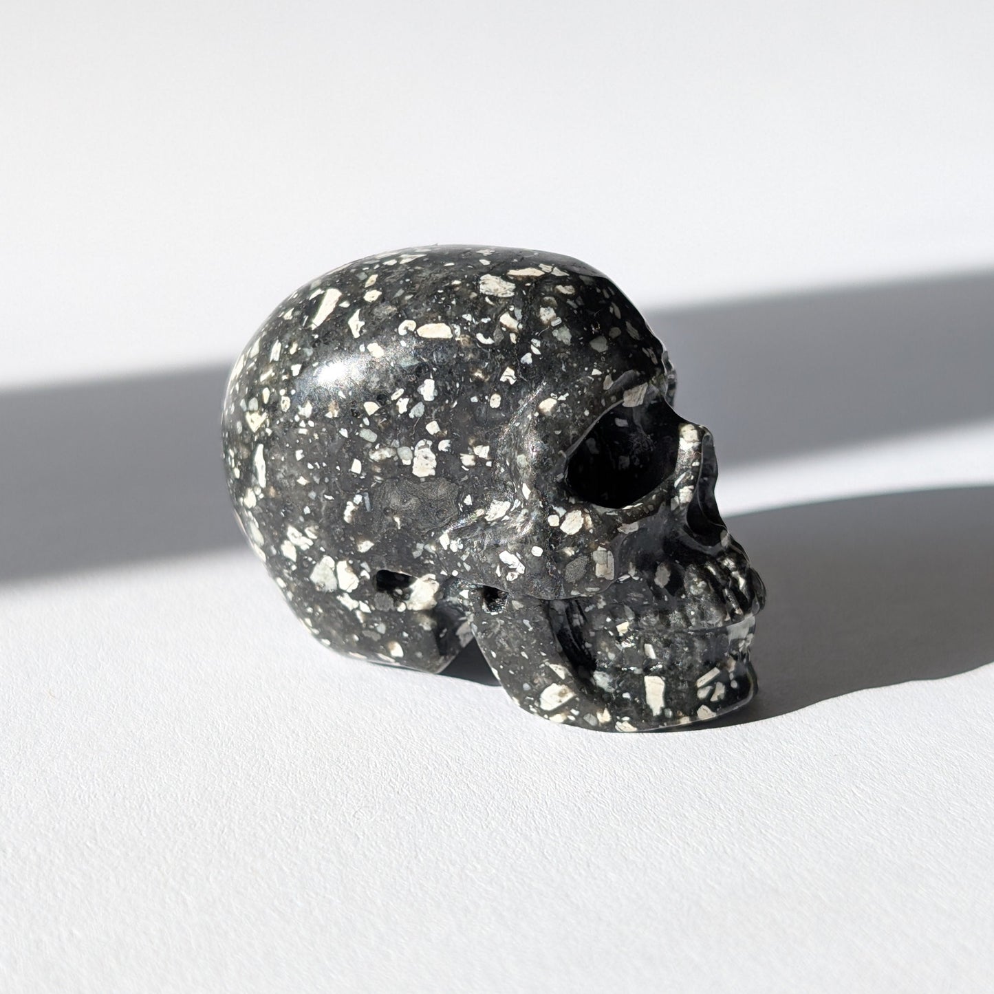 Kleiner Kristallschädel "Blyss" (87g) aus dunkelgrauem Gabbro (Mystic Merlinite) mit hellen Sprenkeln.