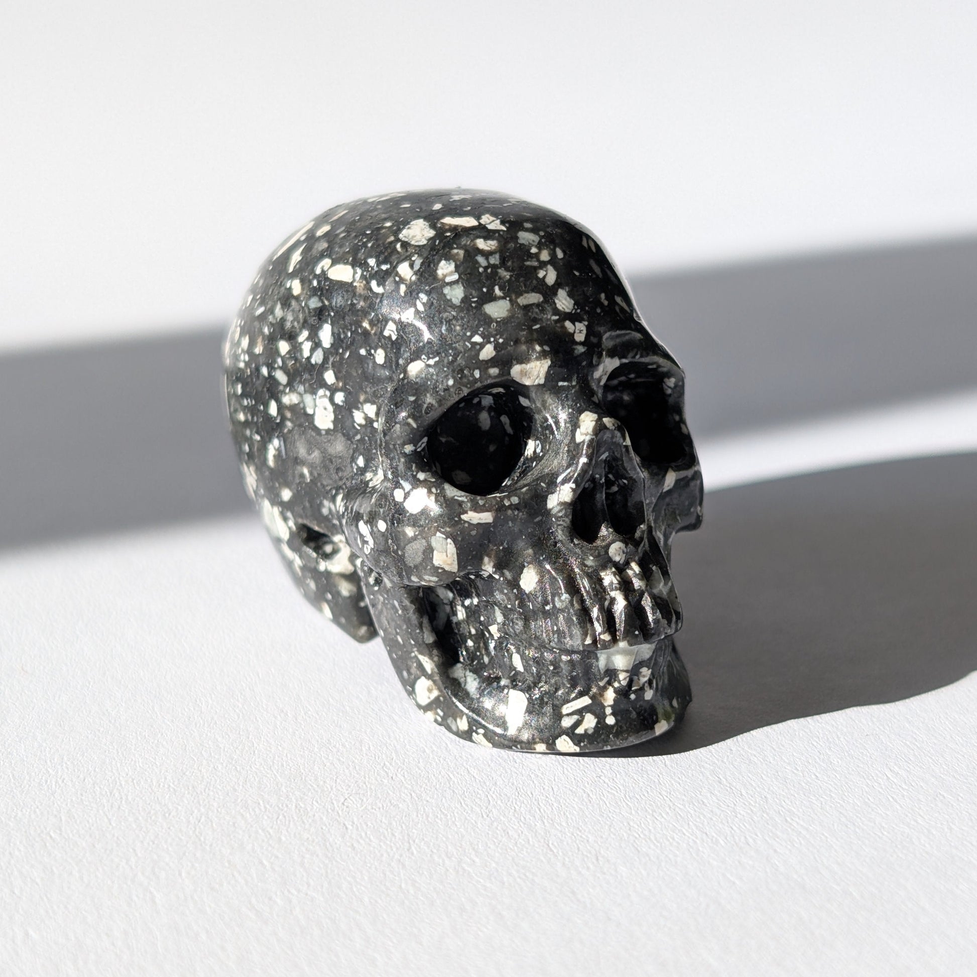 Kleiner Kristallschädel "Blyss" (87g) aus dunkelgrauem Gabbro (Mystic Merlinite) mit hellen Sprenkeln.