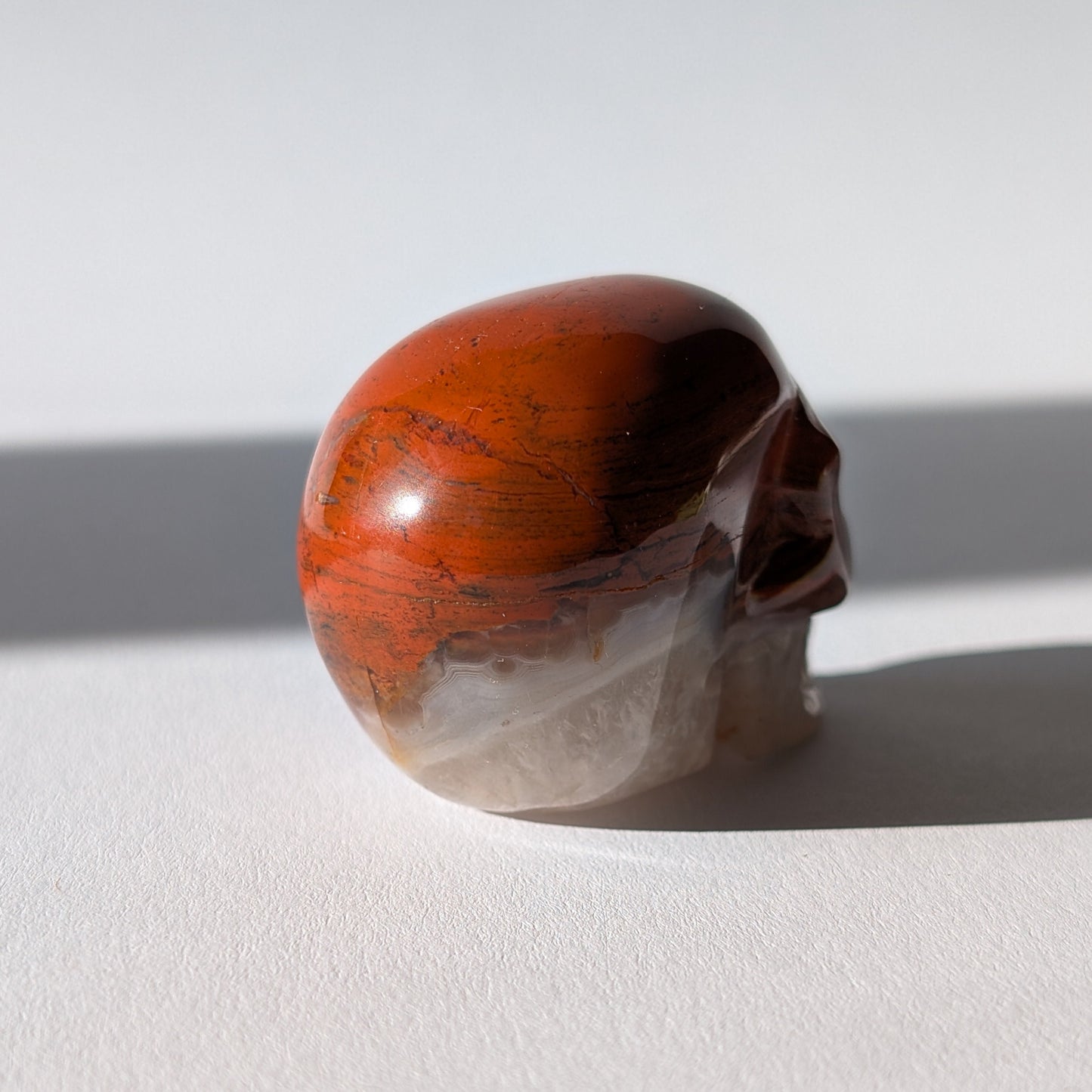 Kleiner Kristallschädel "Edun" (86g), halb aus rotem Jaspis, halb aus hellem Quarz.