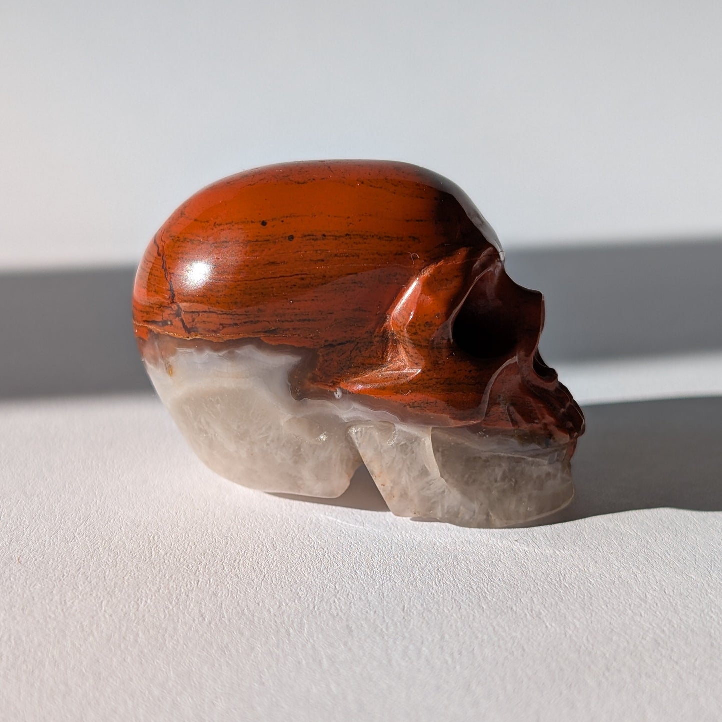 Kleiner Kristallschädel "Edun" (86g), halb aus rotem Jaspis, halb aus hellem Quarz.