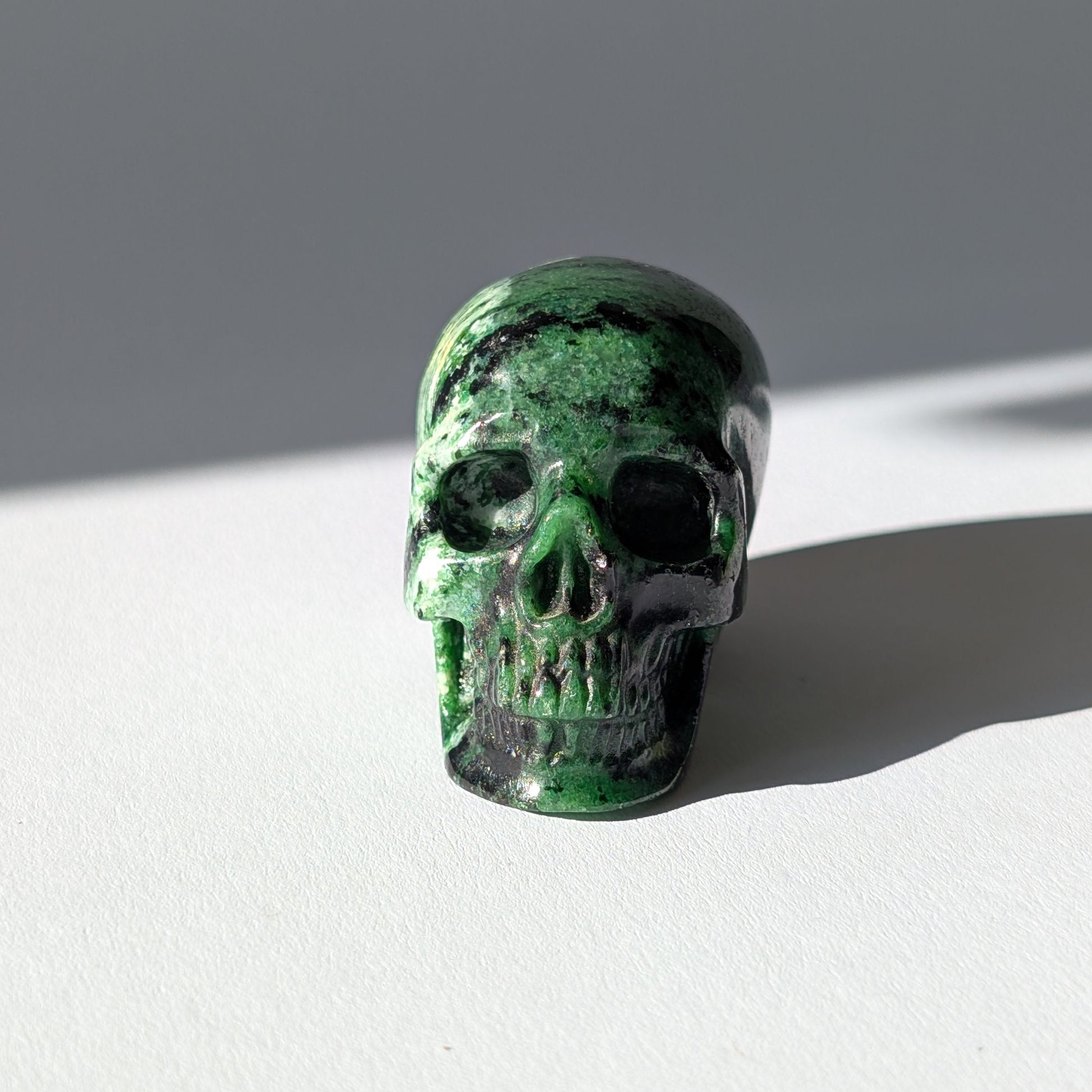 Kleiner Kristallschädel "Leonidar" (92g) aus grünem Zoisit mit schwarzen Einschlüssen.