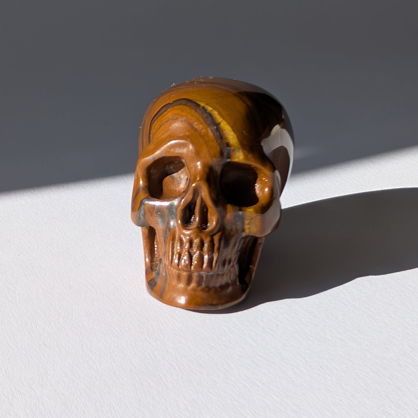 Kleiner Kristallschädel "Rogras" (104g) aus gebändertem Tigereisen mit goldener Chatoyancy.