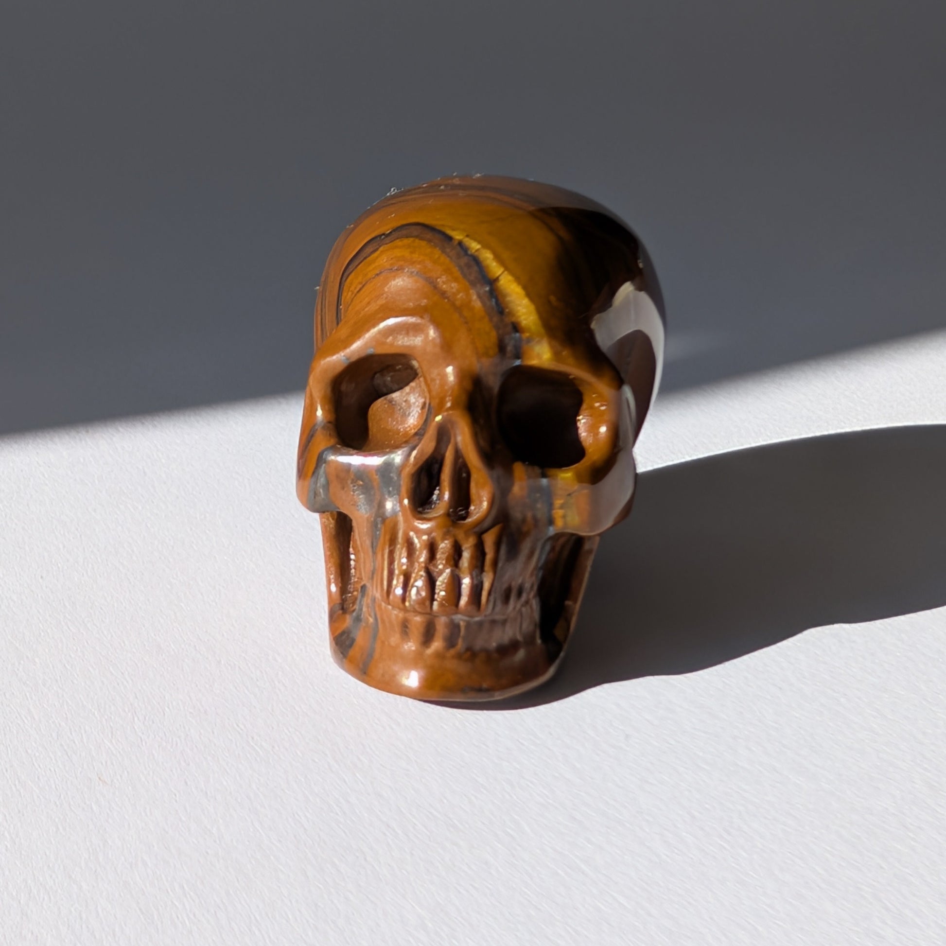 Kleiner Kristallschädel "Rogras" (104g) aus gebändertem Tigereisen mit goldener Chatoyancy.