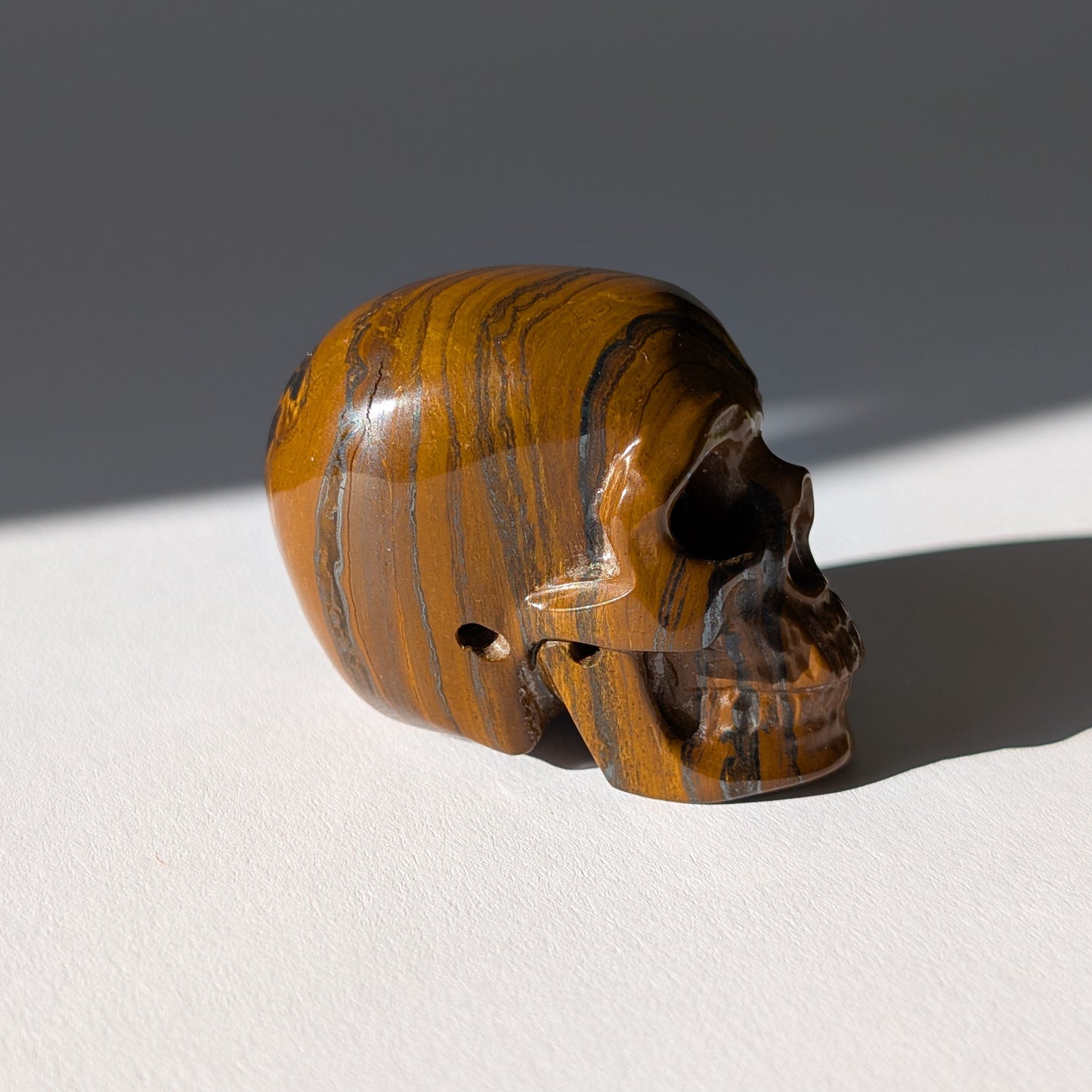 Kleiner Kristallschädel "Rogras" (104g) aus gebändertem Tigereisen mit goldener Chatoyancy.