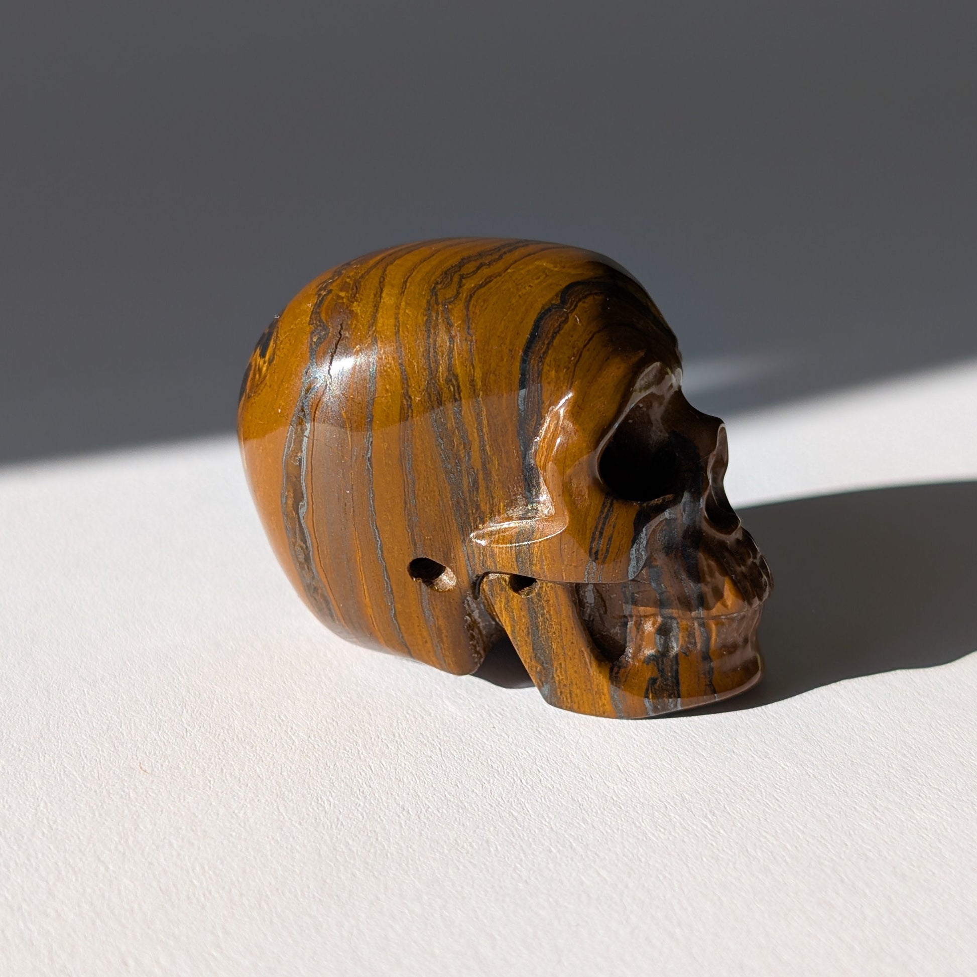 Kleiner Kristallschädel "Rogras" (104g) aus gebändertem Tigereisen mit goldener Chatoyancy.