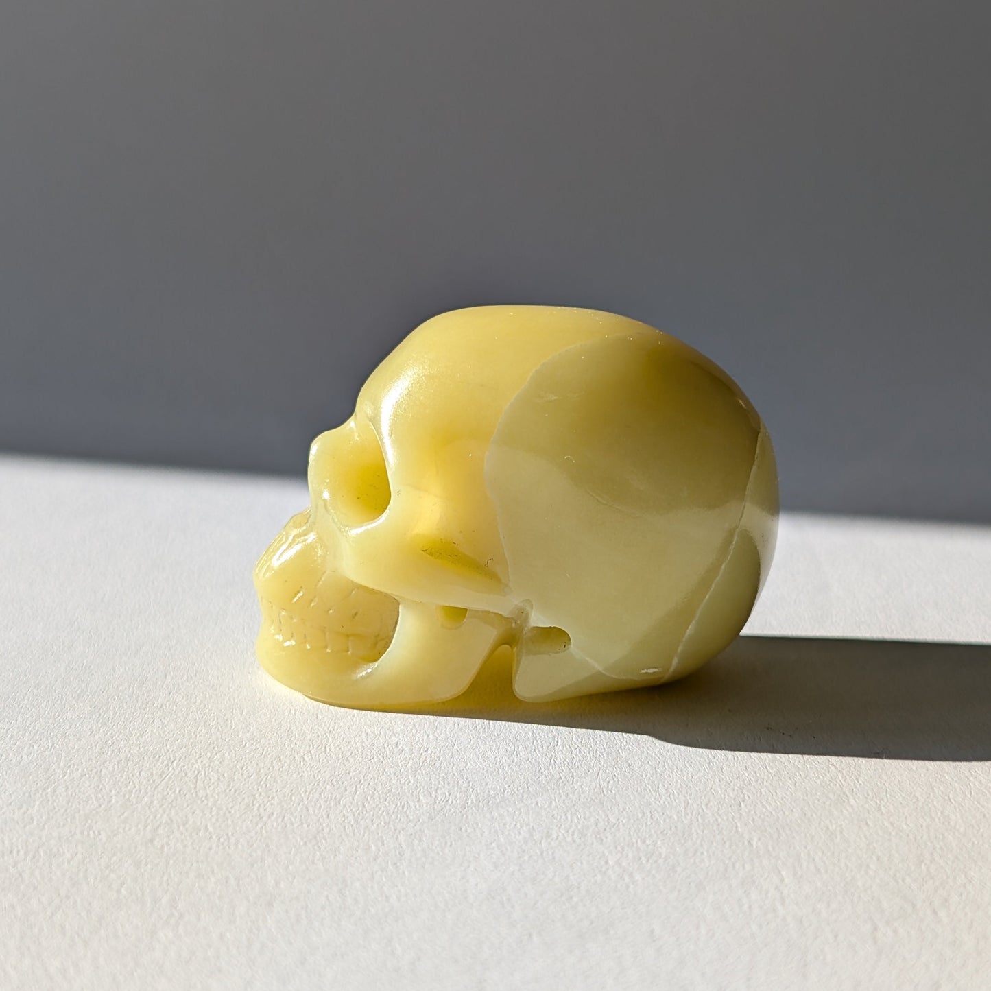 Kleiner Kristallschädel "Sentos" (78g) aus blassgrün-gelbem Jadeit im Licht.