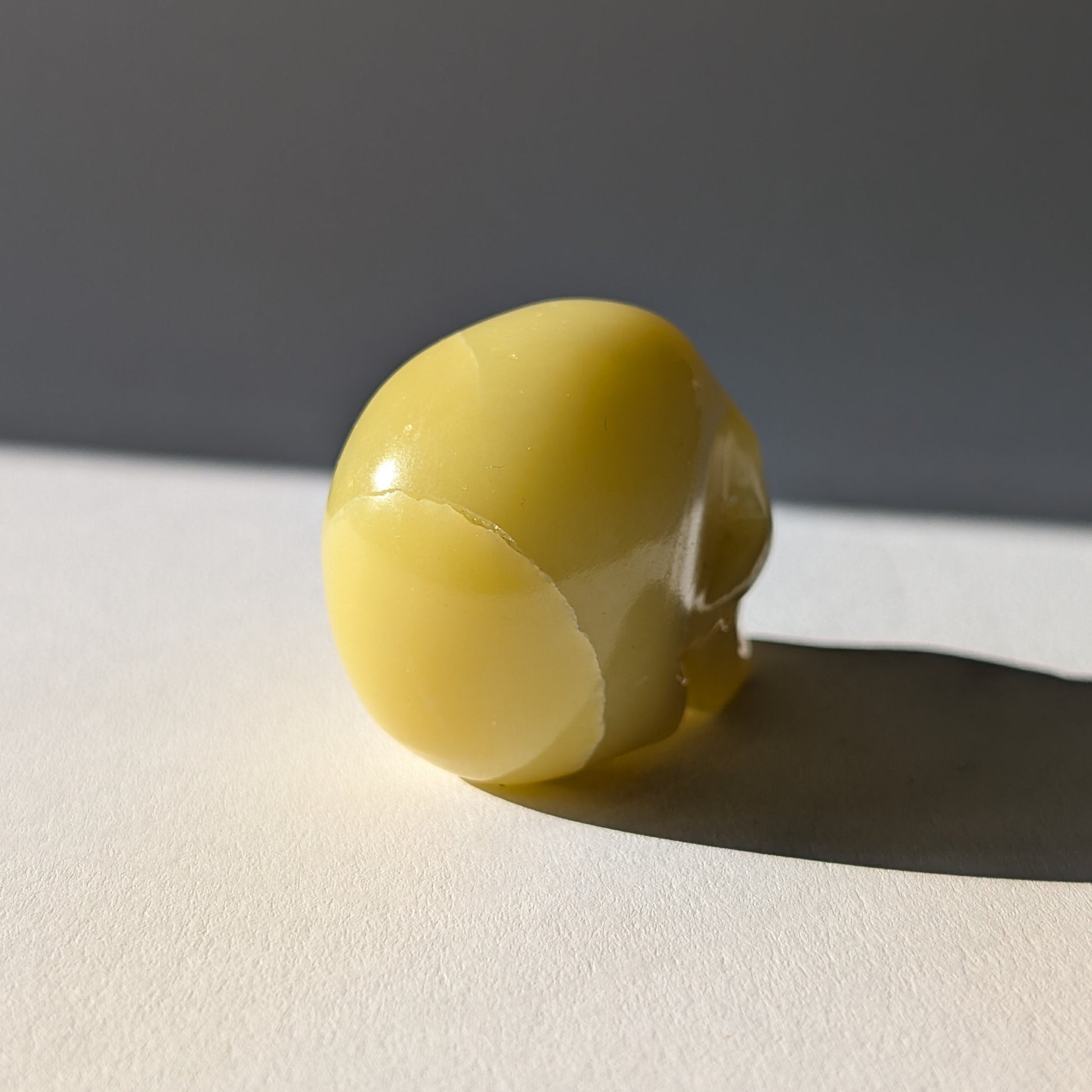 Kleiner Kristallschädel "Sentos" (78g) aus blassgrün-gelbem Jadeit im Licht.