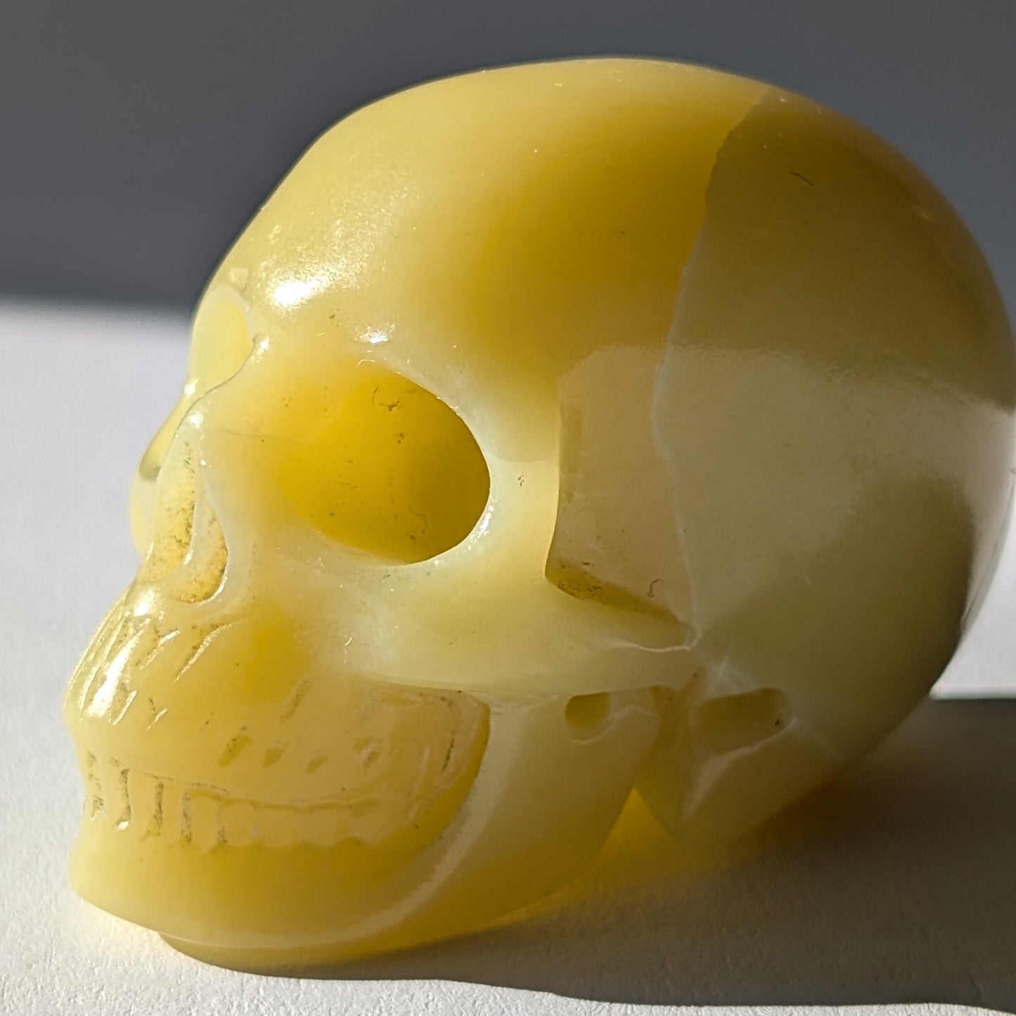 Kleiner Kristallschädel "Sentos" (78g) aus blassgrün-gelbem Jadeit im Licht.