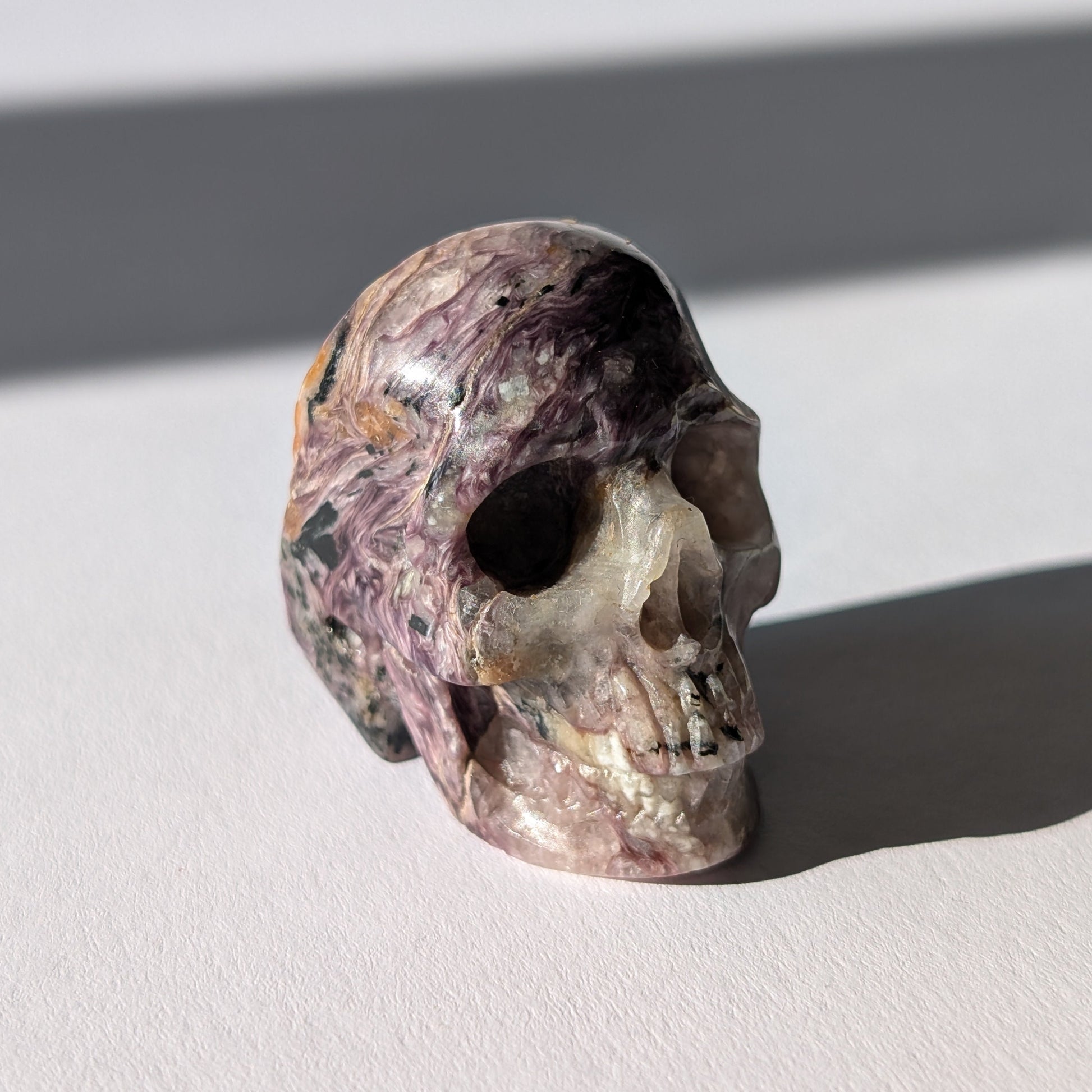 Kleiner Kristallschädel "Veykor" (51g) aus violettem Charoit mit seidigen Wirbeln.