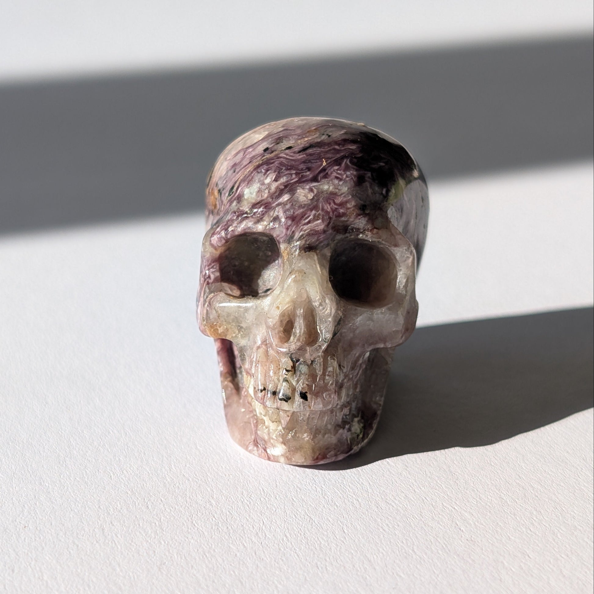 Kleiner Kristallschädel "Veykor" (51g) aus violettem Charoit mit seidigen Wirbeln.