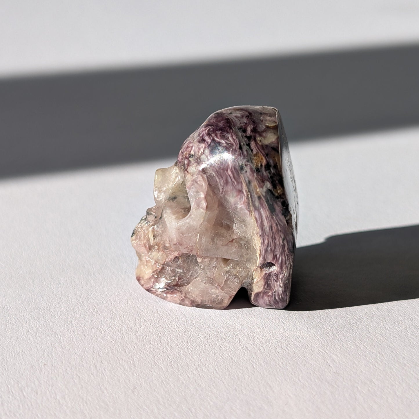 Kleiner Kristallschädel "Veykor" (51g) aus violettem Charoit mit seidigen Wirbeln.