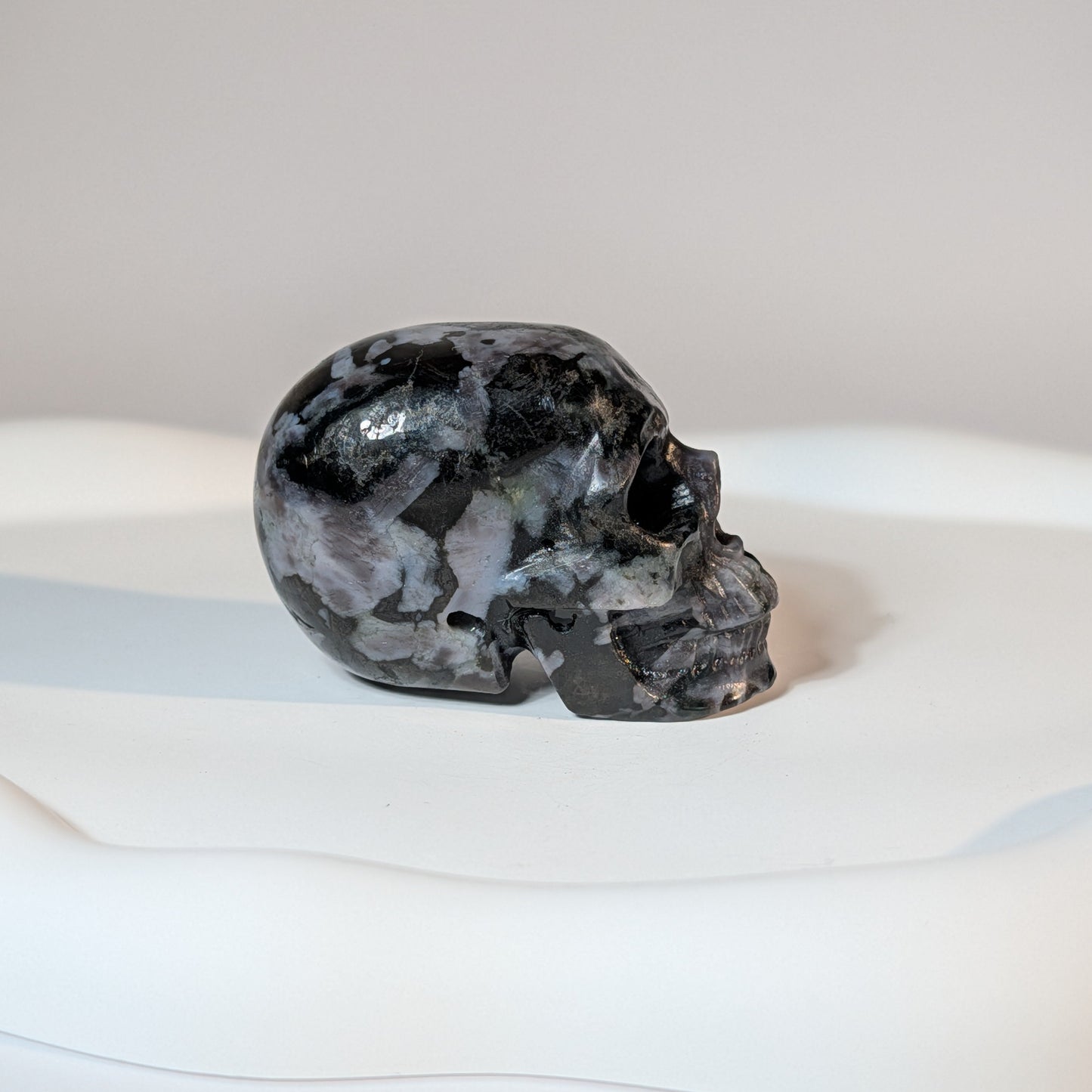 Kompakter Kristallschädel Fayt aus Nephelin, mit einer hellen, von dunklen Mineralien gesprenkelten Gesteinsmatrix.