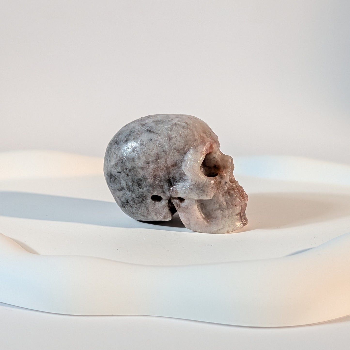 Kristallschädel Armun aus rohem Klinozoisit 92g mit dunklen, natürlichen Einschlüssen und harten Brüchen im kontrastreichen Licht