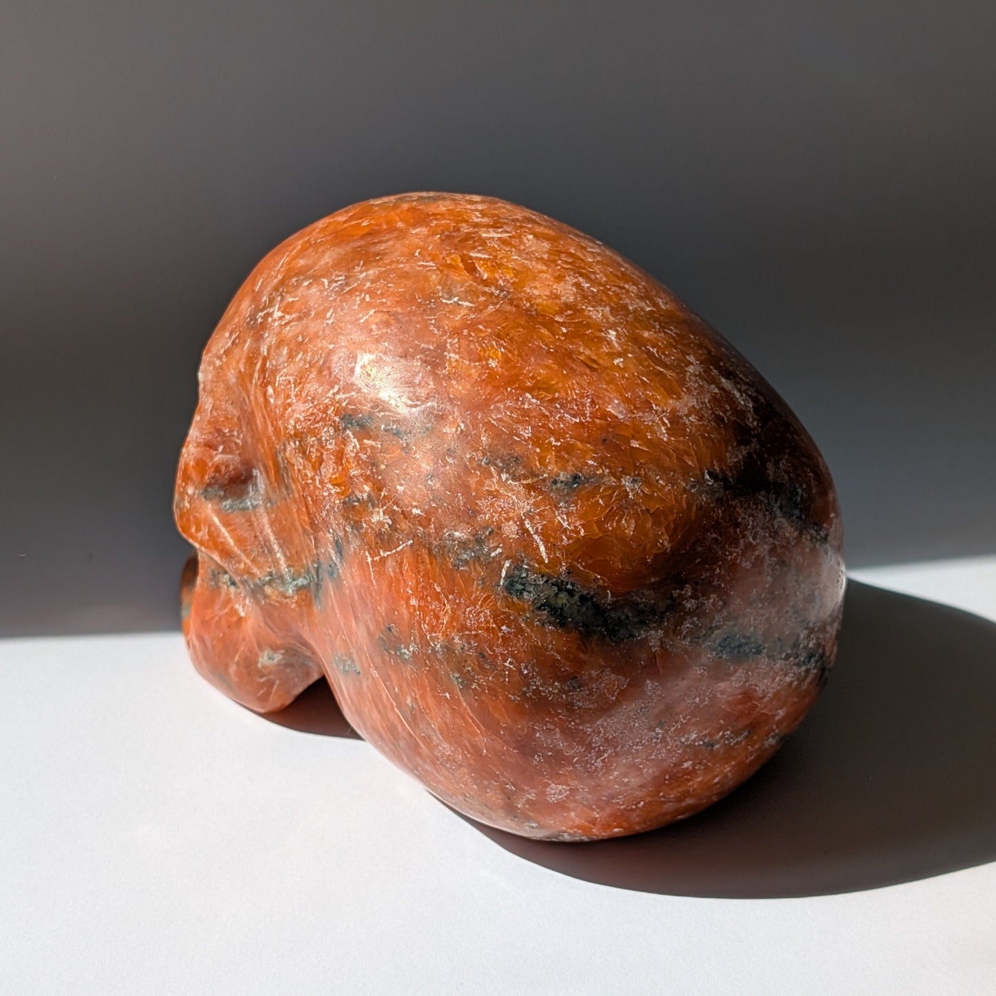 Kristallschädel "Aurelius" aus sonnenorangem Sonnenstein mit dunklen Einschlüssen.
