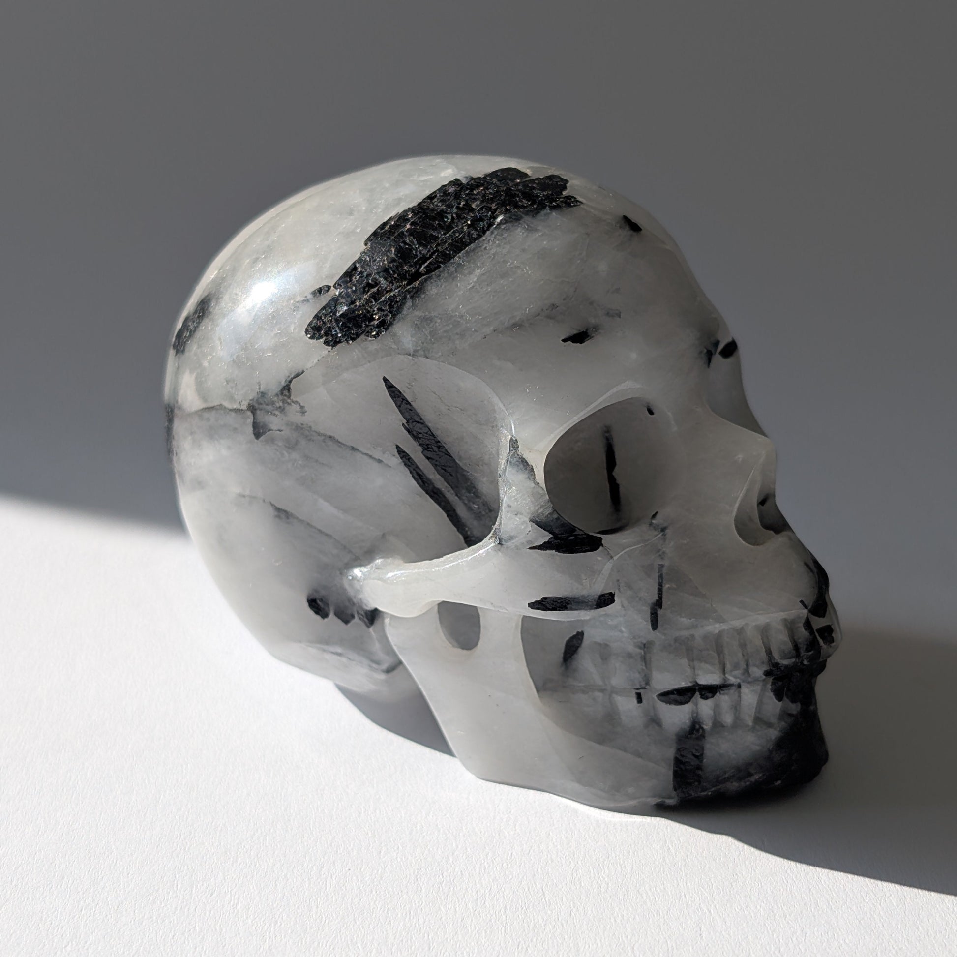 Kristallschädel "Hokan" (436g) aus klarem Quarz mit schwarzen Turmalin-Nadeln.