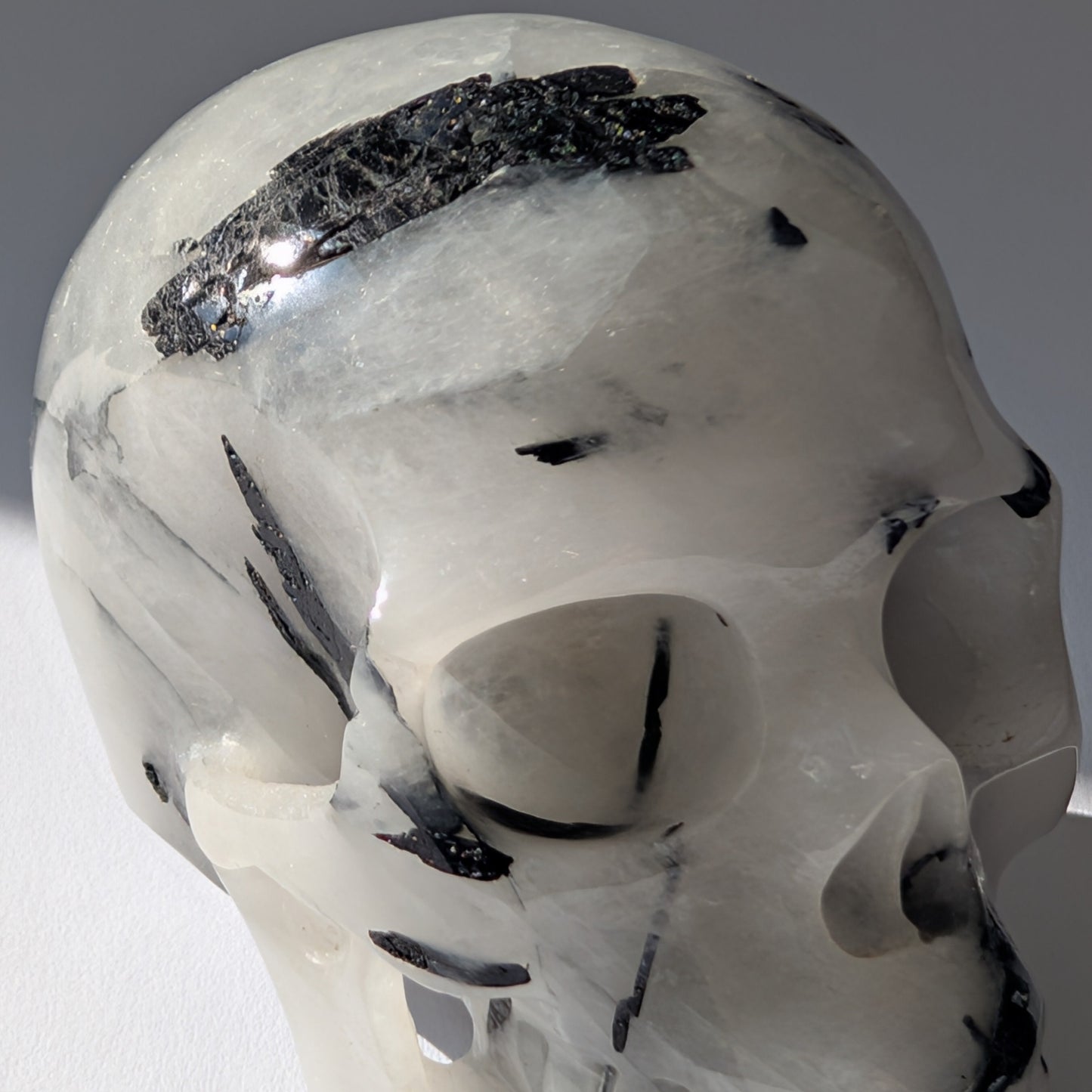 Kristallschädel "Hokan" (436g) aus klarem Quarz mit schwarzen Turmalin-Nadeln.