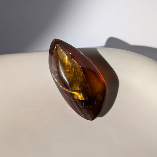 Kunstvoll geschliffener Bicolor-Bernstein 'Die Flamme der Vorzeit' in eleganter Flammenform, der von tiefrot zu gold leuchtet.