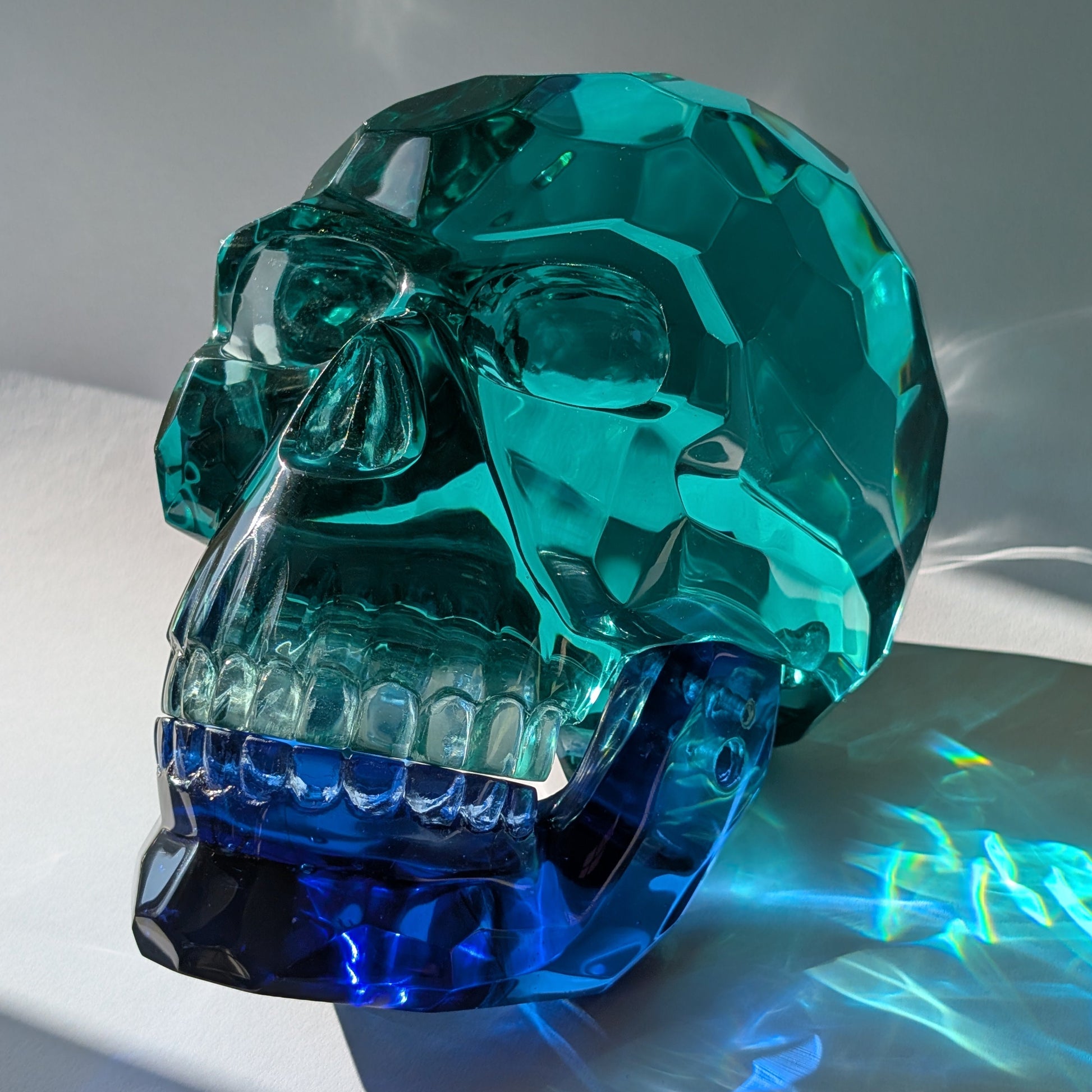 Monumentaler Kristallschädel (7.5kg) aus facettiertem blaugrünem Glas mit beweglichem Unterkiefer im Lichtspiel.