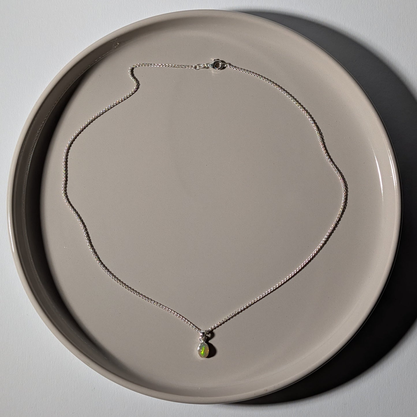 Polierter ovaler Opal Anhänger mit leuchtendem Farbspiel in einer schlichten 925er Silberfassung an einer Silberkette, energetisch aufgeladen von Temple of Desire