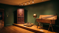 Museumsraum mit historischen Zauberrequisiten: Verschwindeschrank mit Sternen, Ketten mit Vorhängeschlössern, schwebende Messingkugel und Sägekiste – KI-Illustration, nicht die Ausstellung