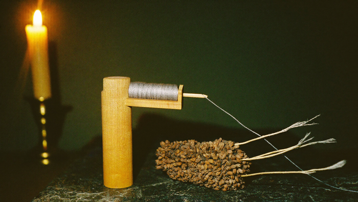 Holzspindel mit silbergrauem Faden und trockener Samenstand auf dunklem Stein im Kerzenlicht