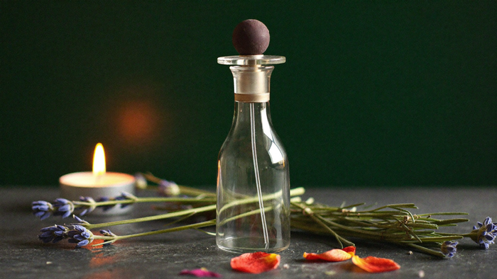 Glasflakon mit Zerstäuber zwischen Lavendelzweigen und Rosenblättern neben einer Kerze