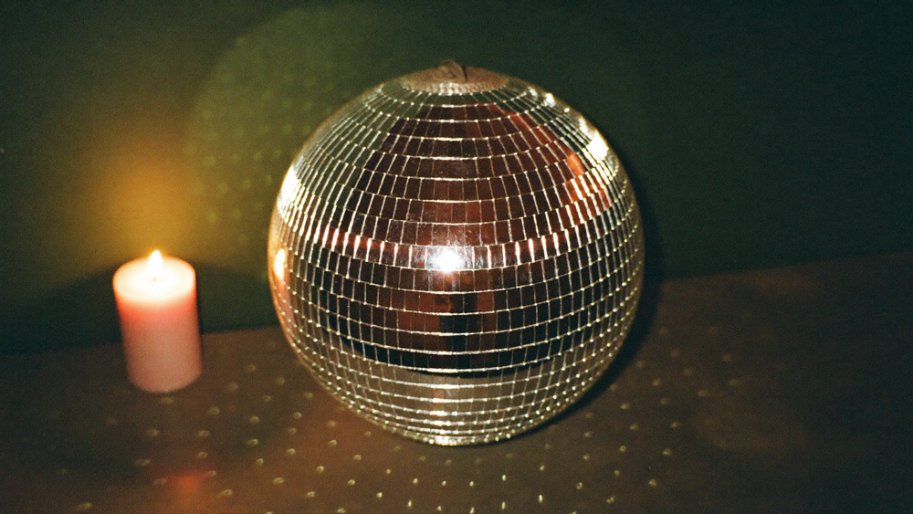 Eine Spiegelkugel auf dunkler Fläche neben einer brennenden Kerze, Lichtpunkte auf dunkelgrüner Wand