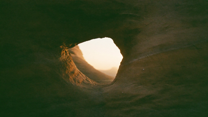Rundes Loch in einer verwitterten Sandsteinwand, durch das warmes Morgenlicht auf den Stein fällt