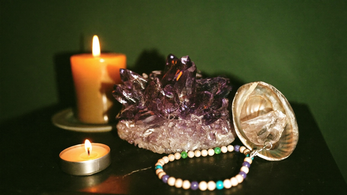 Amethystdruse, Bergkristall und Abalone-Muschel mit einem Edelstein-Armband auf dunklem Stein bei Kerzenlicht