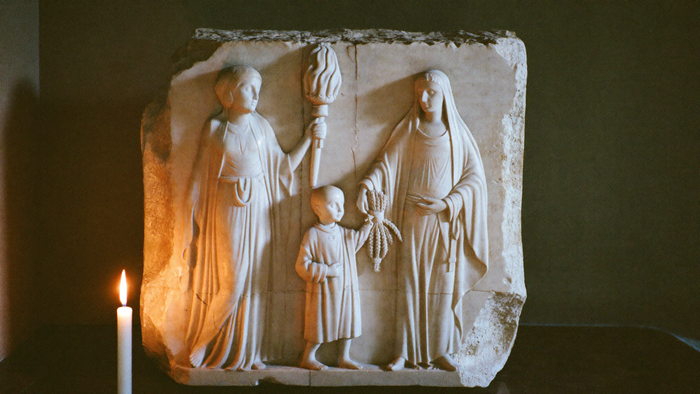 Marmorrelief im Kerzenlicht: eine Göttin mit Fackel, eine zweite reicht einem Knaben ein Bündel Ähren — Demeter, Persephone und Triptolemos
