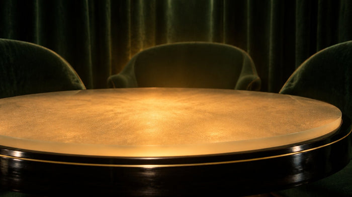 Runder Séance-Tisch mit von unten leuchtender Milchglasplatte, dahinter leere grüne Samtsessel und ein dunkler Vorhang