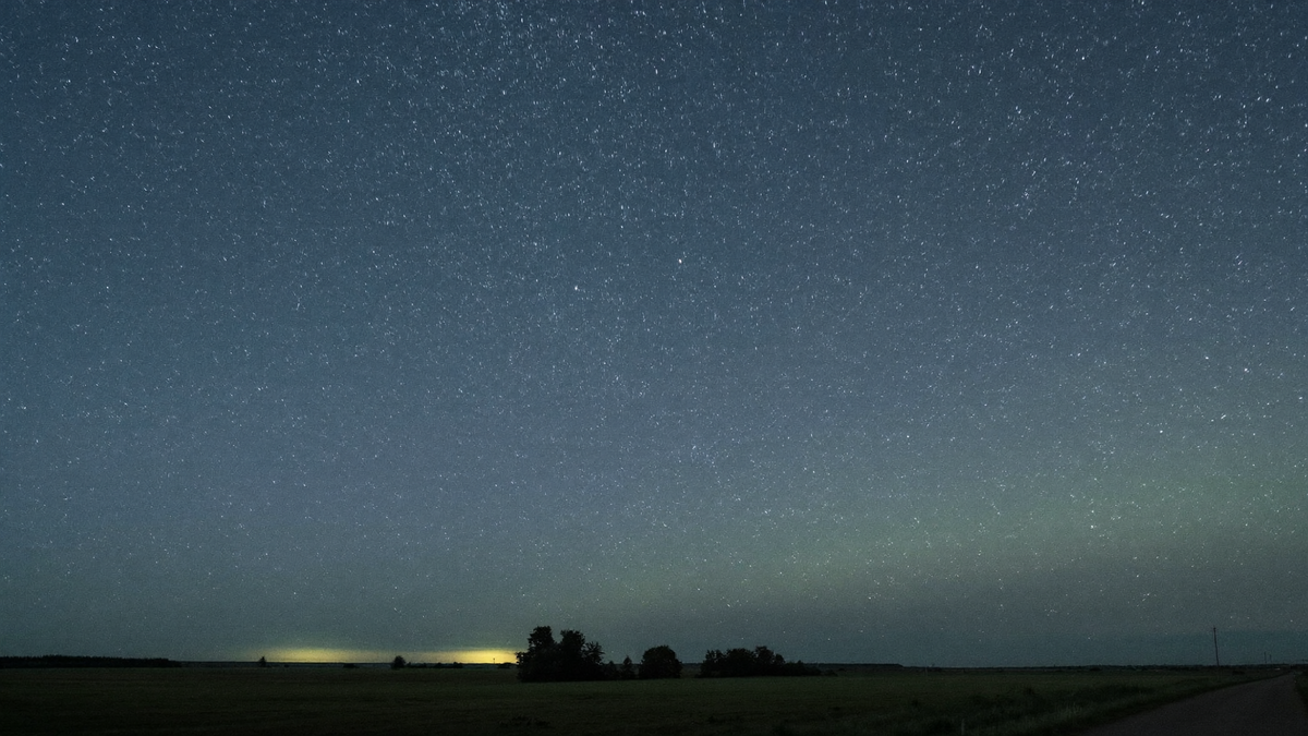 Sternenhimmel über flacher norddeutscher Feldlandschaft, am Nordhorizont ein schwacher grünlicher Schimmer