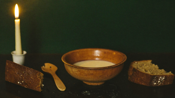 Schale mit Milch, Brotkanten und Holzlöffel bei Kerzenlicht — die überlieferte Gabe für den Hausgeist