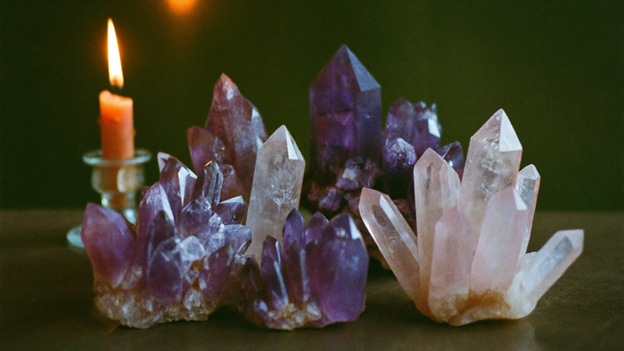 Amethyst- und Rosenquarzstufen neben einer brennenden Kerze vor dunkelgrüner Wand