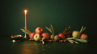 Mabon-Erntealtar zur Herbst-Tagundnachtgleiche: Äpfel, Weizenähren, Haselnüsse und eine Messingschale im Kerzenlicht vor dunkelgrüner Wand.