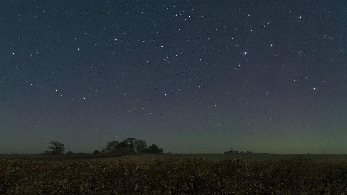 Sternenhimmel über einer flachen norddeutschen Feldlandschaft, am Horizont nur ein sehr schwacher grünlicher Schimmer