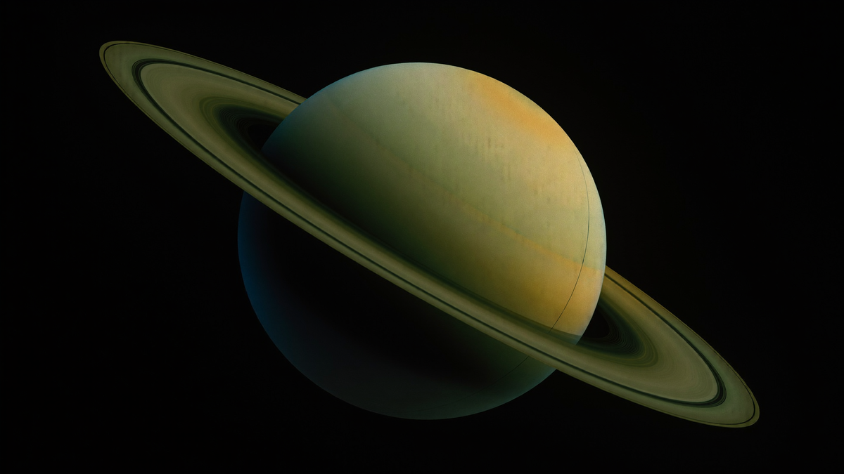 Der Planet Saturn mit geneigtem Ringsystem vor schwarzem Weltraum, der Südpol liegt im Schatten, warmes Bernsteinlicht an der oberen Kante