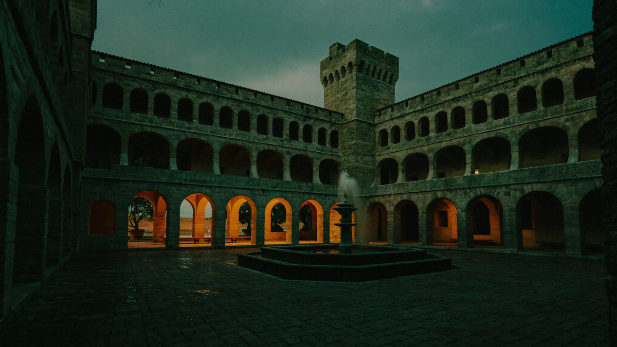 Renaissance-Schlosshof mit drei Arkadengeschossen und einem Brunnen zur blauen Stunde, warmes Licht fällt von einer Seite durch die Bögen