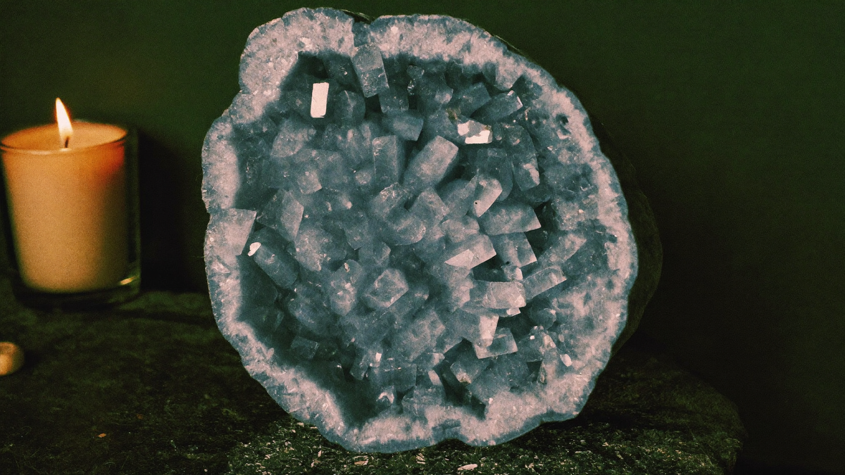 Hellblaue Coelestin-Geode mit glasigen Kristallen auf dunklem Stein bei Kerzenlicht vor dunkelgrüner Wand