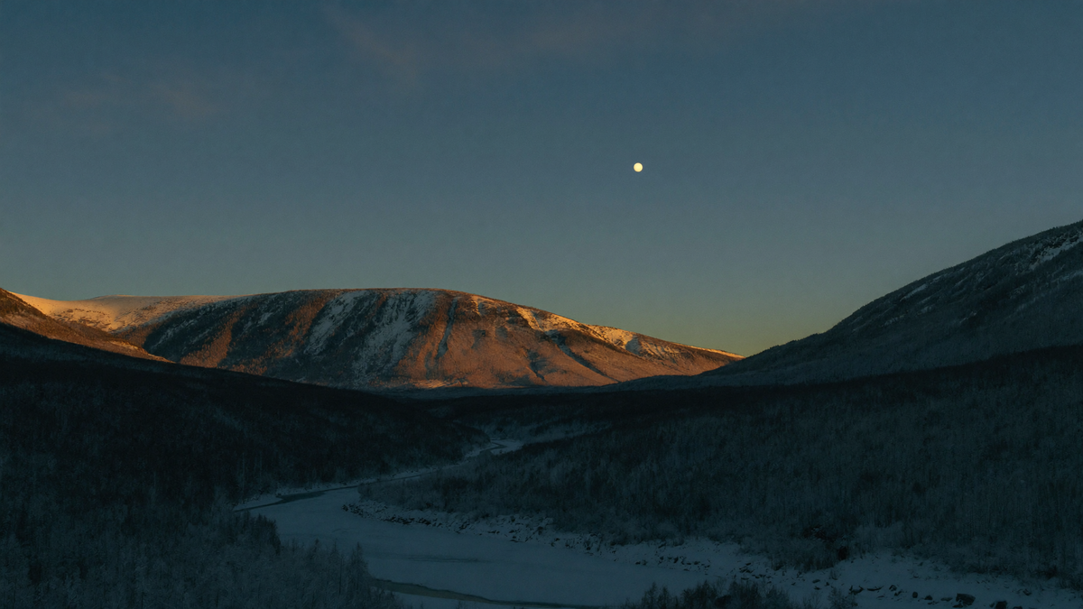 Ein verschneites norwegisches Hochtal zur blauen Stunde, ein gefrorener Fluss im Talgrund, über dem fernen Bergrücken ein einzelnes blasses Licht