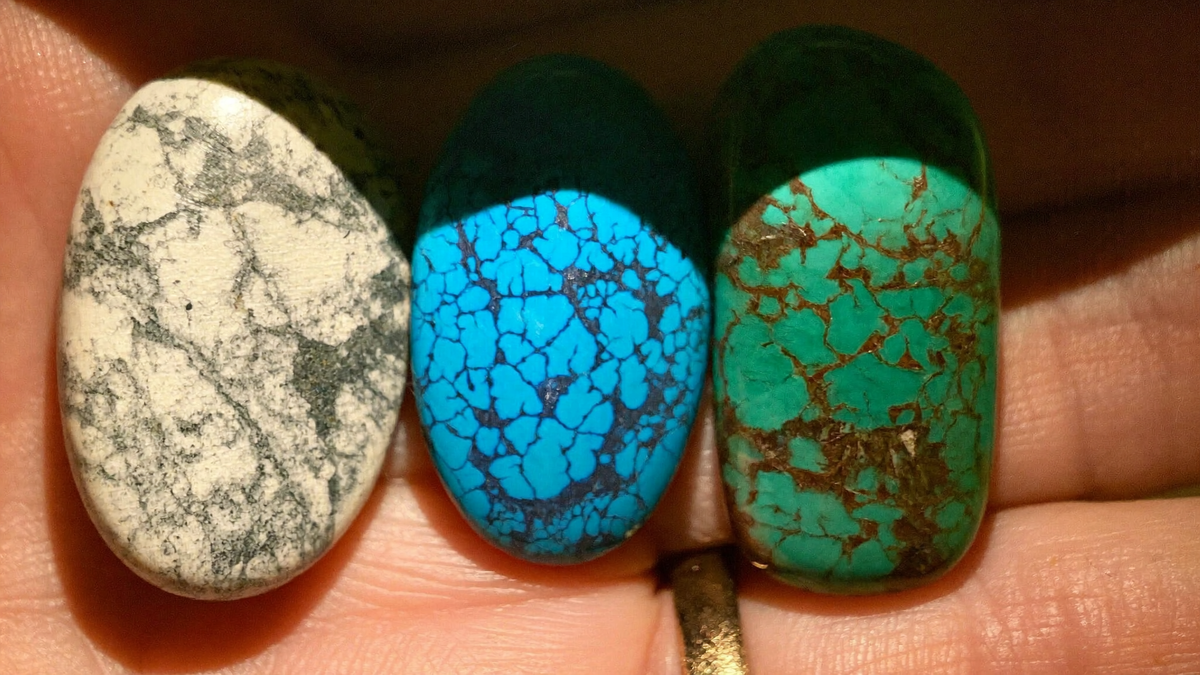 Drei Trommelsteine in einer Hand im Vergleich: weißer Magnesit mit grauen Adern, blau gefärbter Magnesit als Türkis-Imitat und echter Türkis mit brauner Matrix