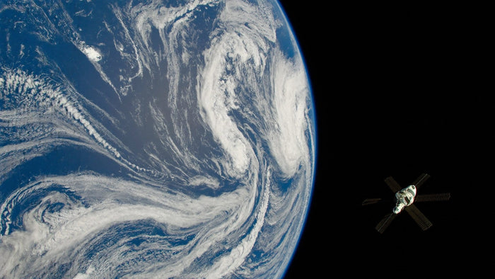 Illustration: Die Erde füllt das Bild mit blauem Ozean und Wolkenwirbeln, rechts davon im schwarzen All eine kleine Raumsonde mit Solarflächen beim Vorbeiflug (KI-generiert)