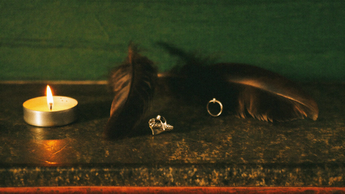 Schwarze Krähenfedern und ein Silberring im Kerzenlicht auf dunklem Stein